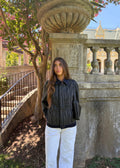 Divine 144 black pinstripe canvas jacket with dark denim collar worn by a woman in a garden setting.