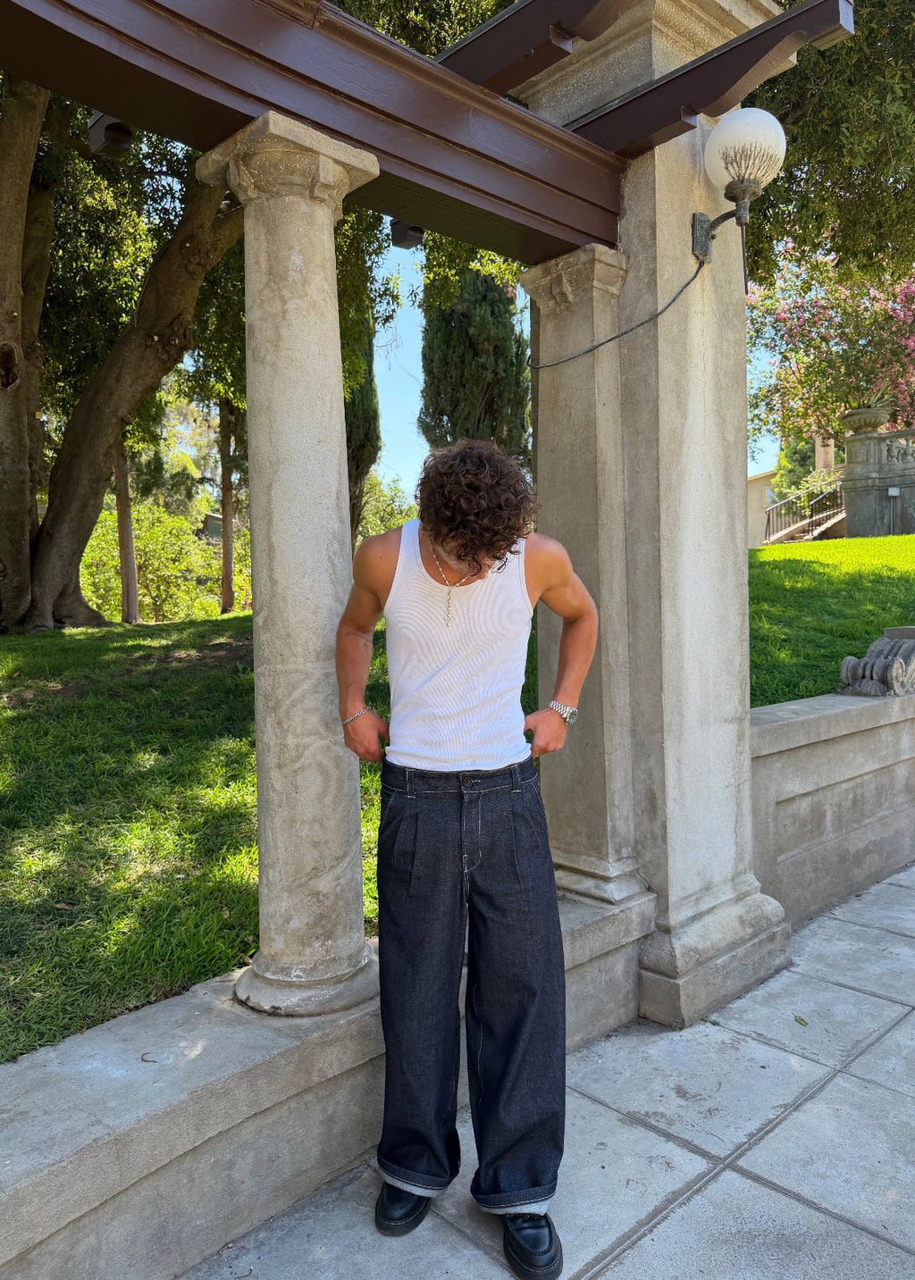 Divine 144 dark indigo raw denim double pleated trousers with a wide straight-leg fit worn by a man in a white tank top