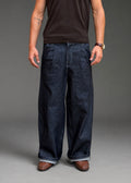 Divine 144 dark indigo raw denim double pleated trousers with a wide straight-leg fit worn by a man.