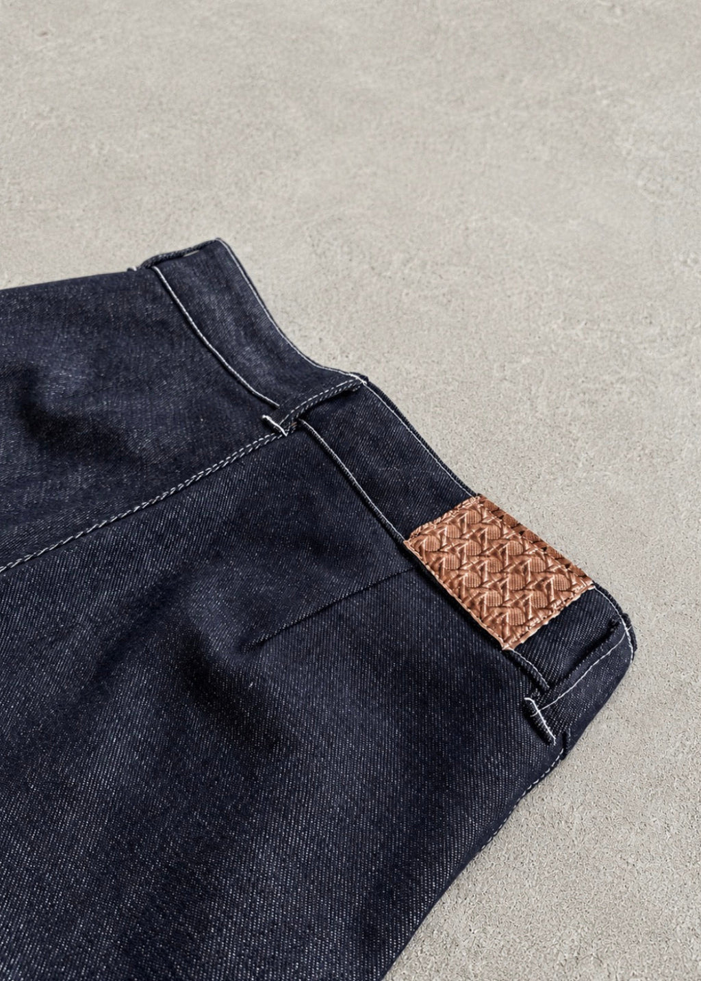 Divine 144 dark indigo raw denim trousers featuring a detailed leather patch with a crown of thorns design.