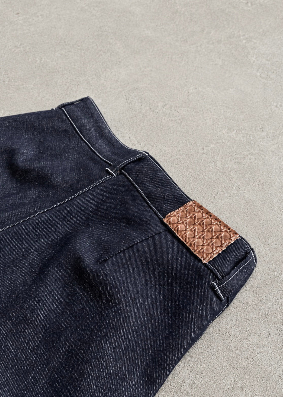 Divine 144 dark indigo raw denim trousers featuring a detailed leather patch with a crown of thorns design.